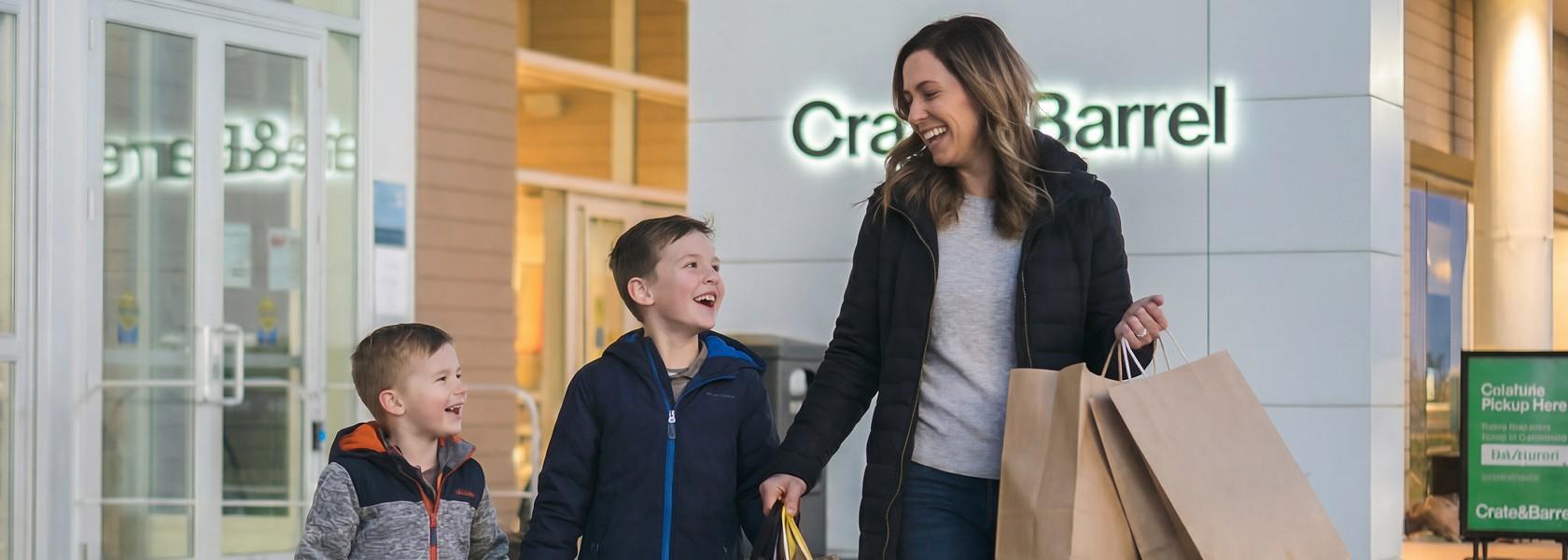 Smiling mother and two boys carrying shopping bags outside Crate & Barrel