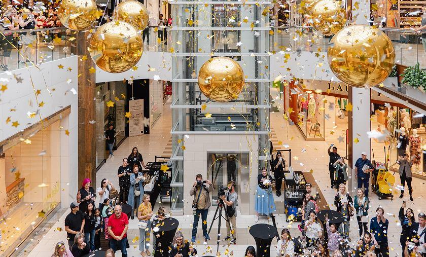 Crowd celebrating under gold balloons and falling confetti in the mall atrium