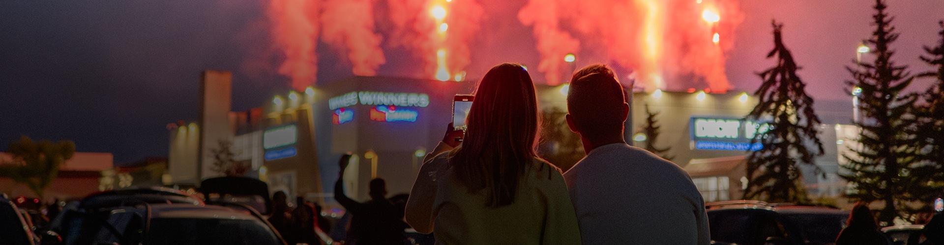 Couple watching fireworks over the mall at night from the parking lot