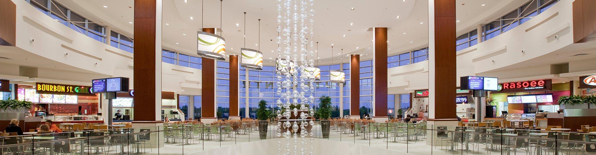 Mall food court at dusk with a tall beaded chandelier and empty tables