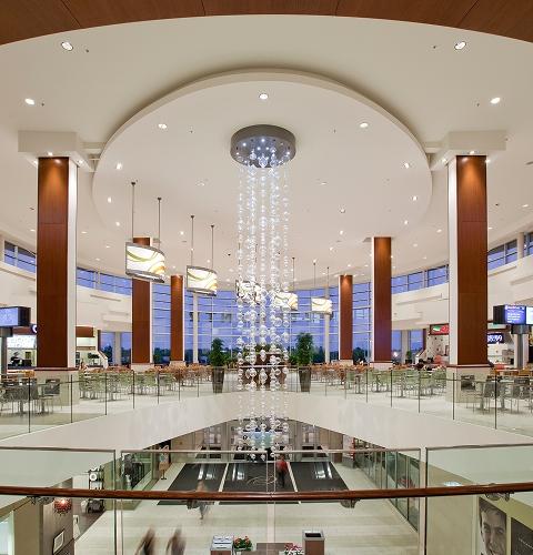Mall food court at dusk with a tall beaded chandelier and empty tables