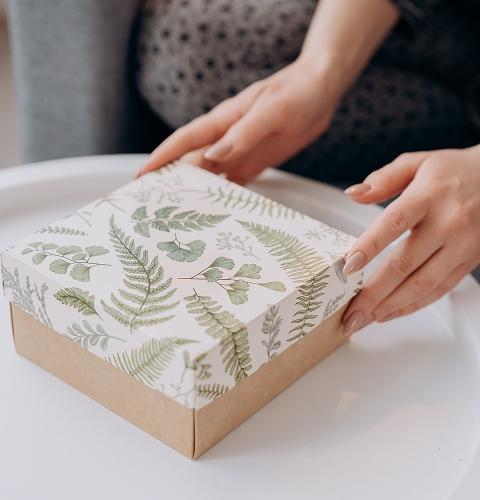 Hands holding a fern-patterned gift box on a white table