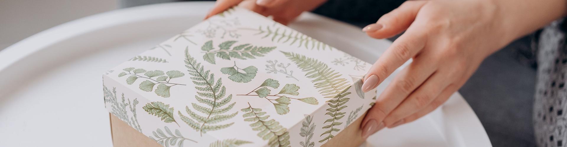 Hands holding a fern-patterned gift box on a white table