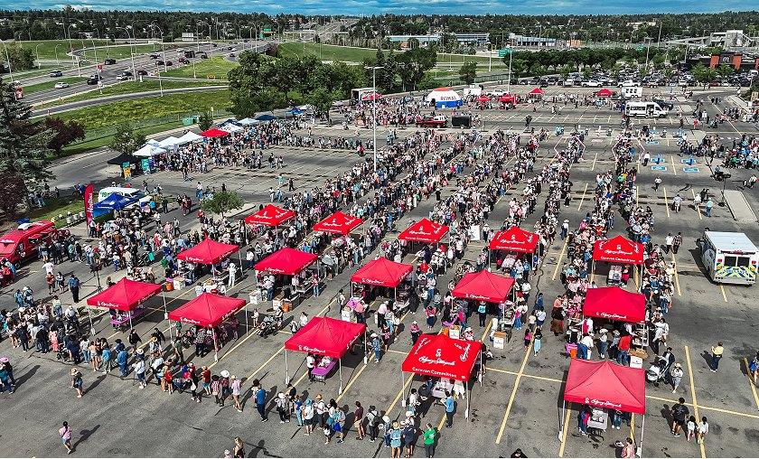 Aerial view of a crowded outdoor festival with red vendor tents in the parking lot