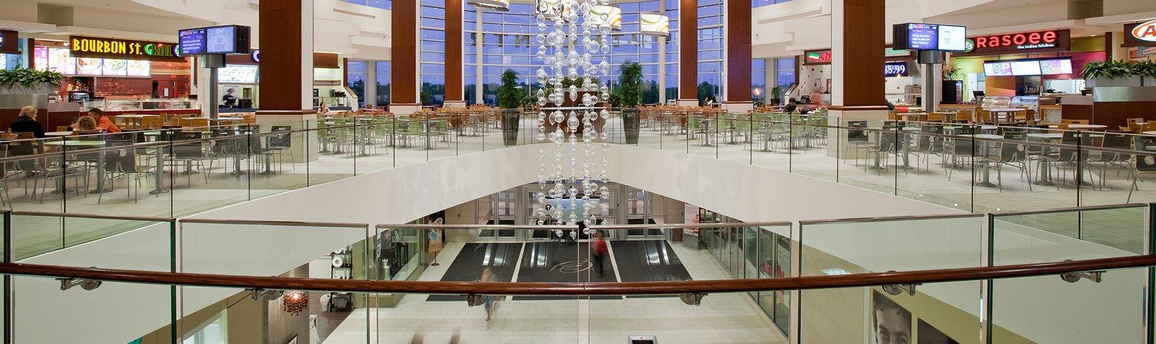 Mall food court balcony with beaded chandelier over escalators at dusk