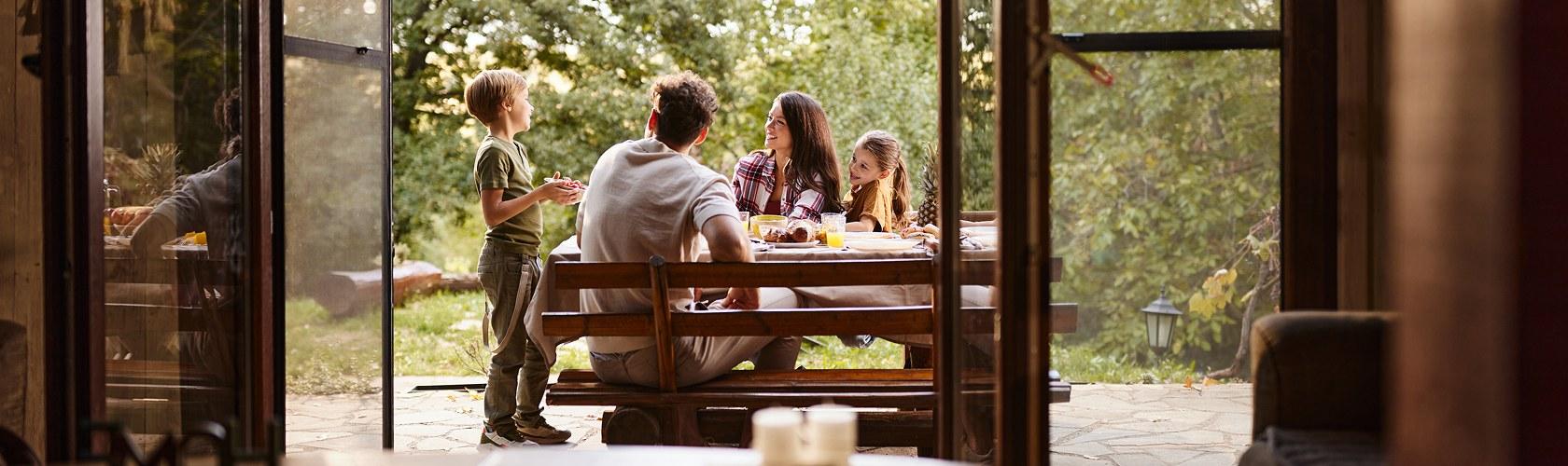 Family dining at an outdoor table seen through open cabin doors