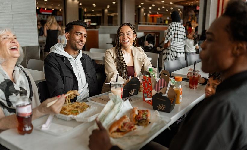 Friends laughing over takeout food at a mall food court table