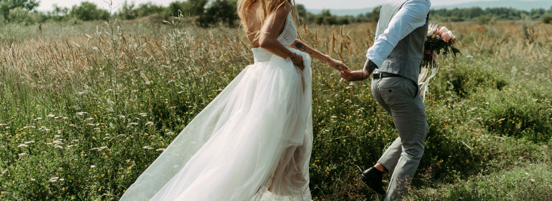 Woman and man in wedding attire running through field