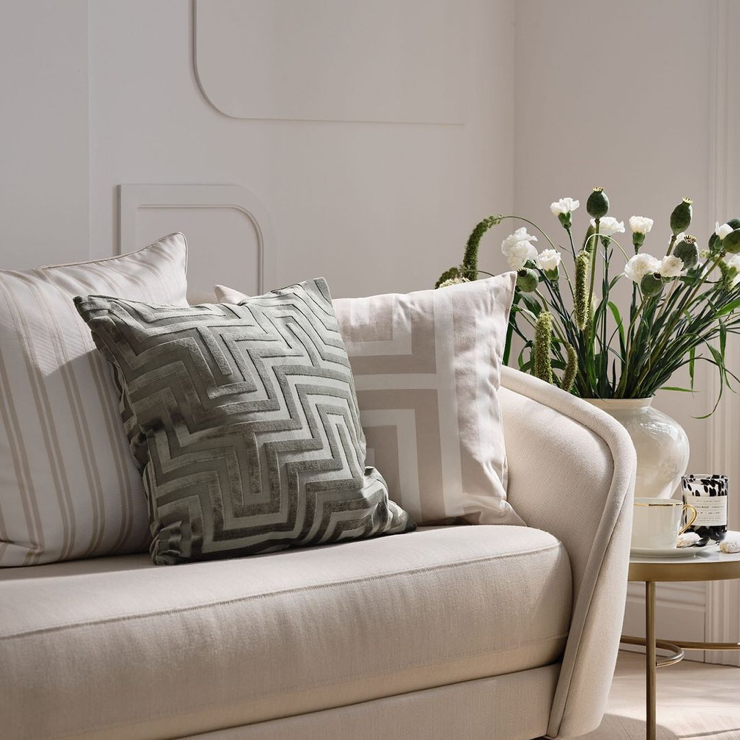 Geometric patterned pillows clustered on a couch with small end table with flowers