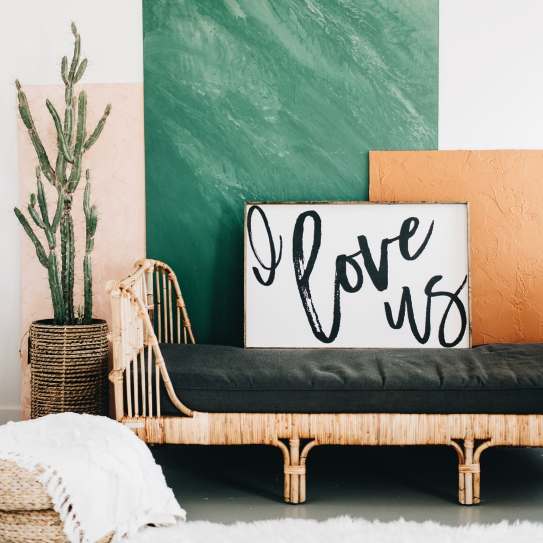 Frame that says "I love us" resting on the wall with a green and orange canvas