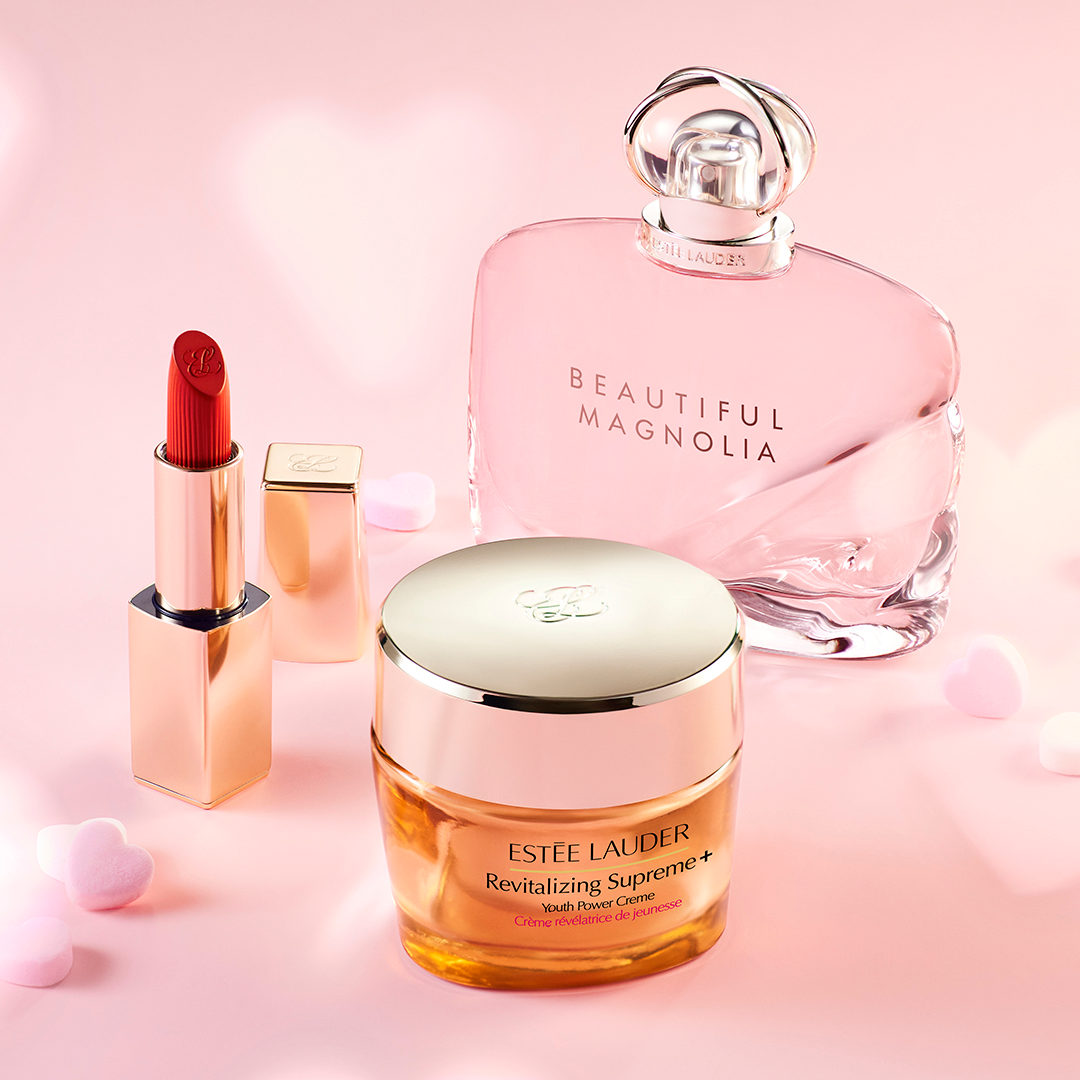 Estee Lauder perfume, lipstick, and creme are displayed on a light pink background.