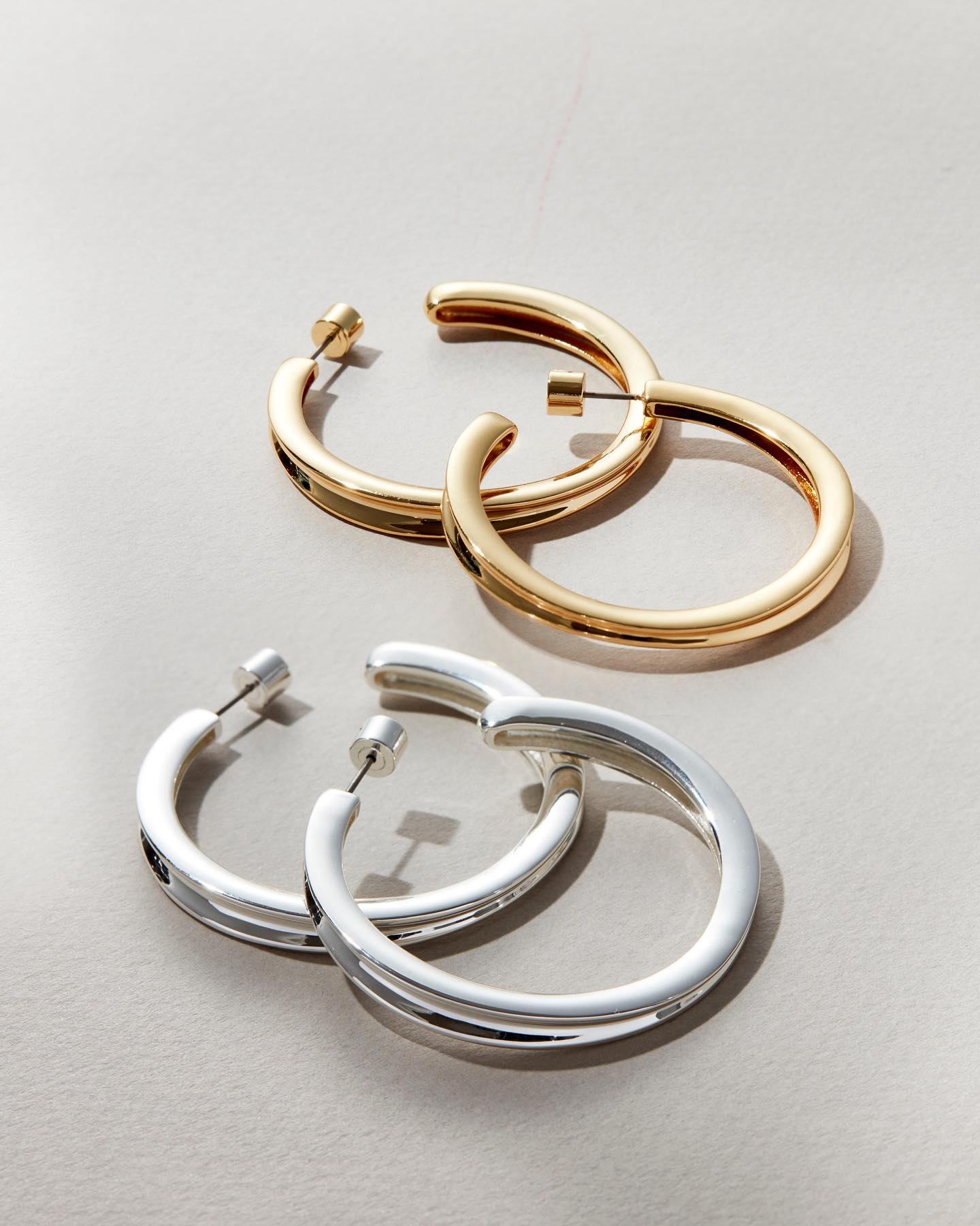 Two pairs of Jenny Bird hoop earrings are laid out. One pair is gold, the other is silver.