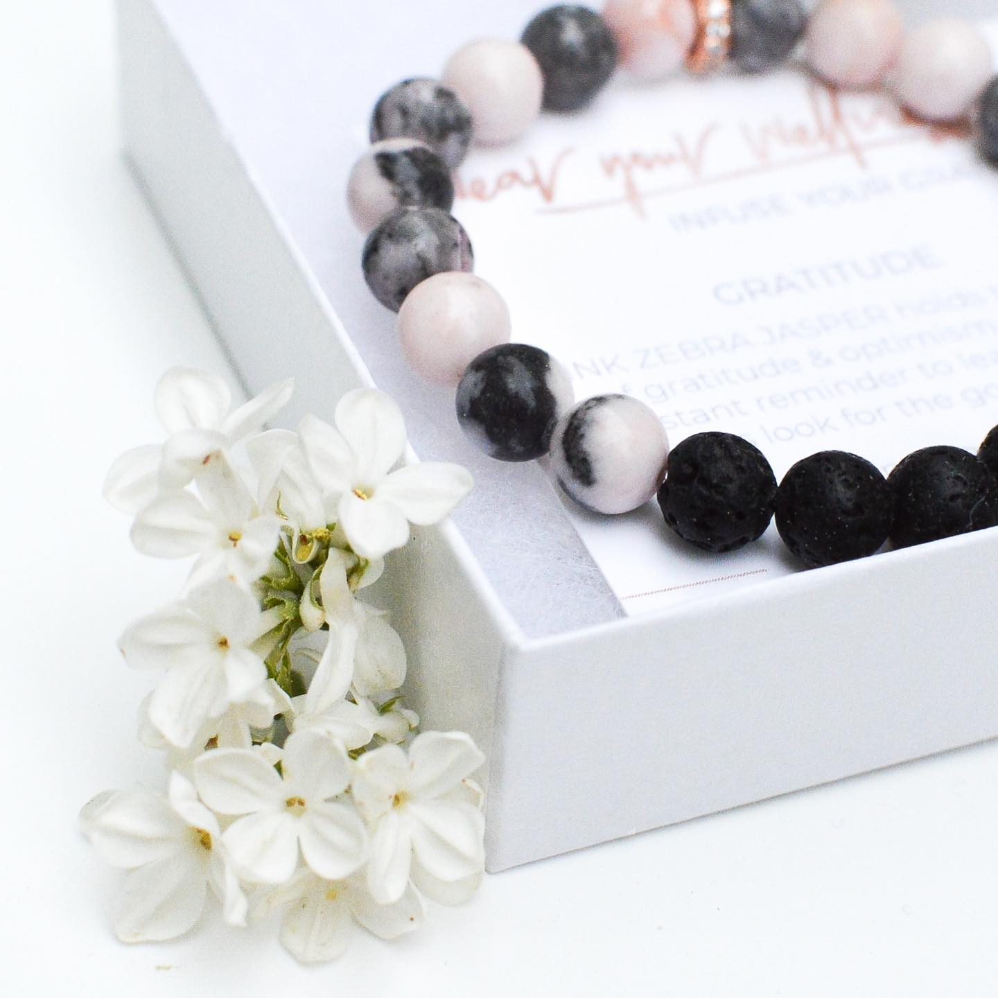 A stone bracelet is in a white box alongside white flowers.
