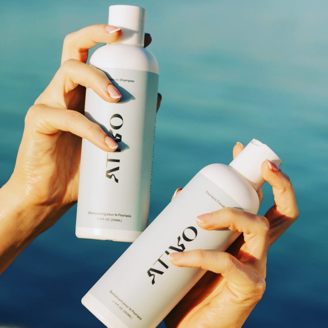 An up close shot of two hands holding two products Oak & Tonic in front of a body of water.