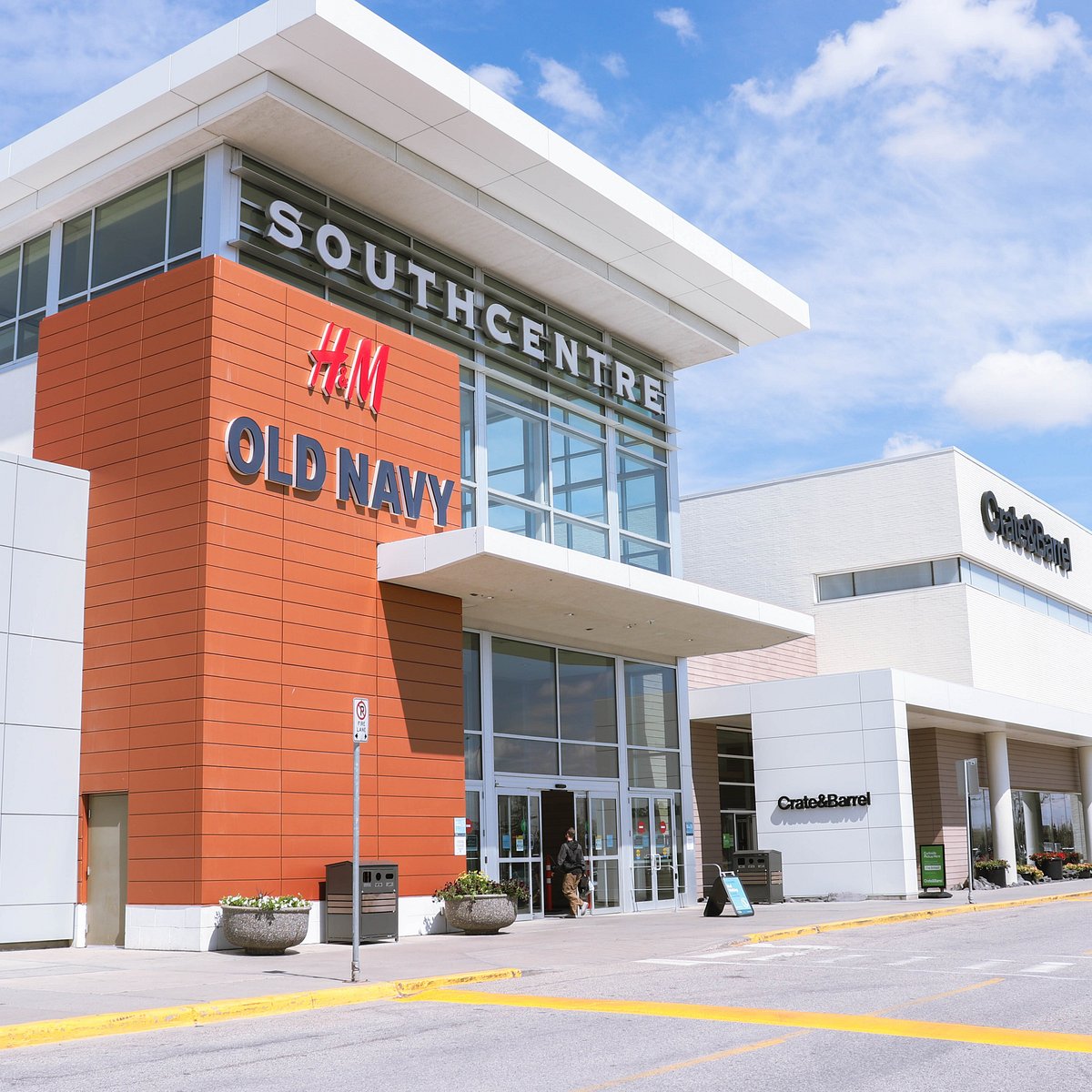 An image of the exterior of Southcentre mall. On the building, there are the logos of H&M, Old Navy and Crate&Barrel. The sky is blue with a few clouds and it's a very sunny day.