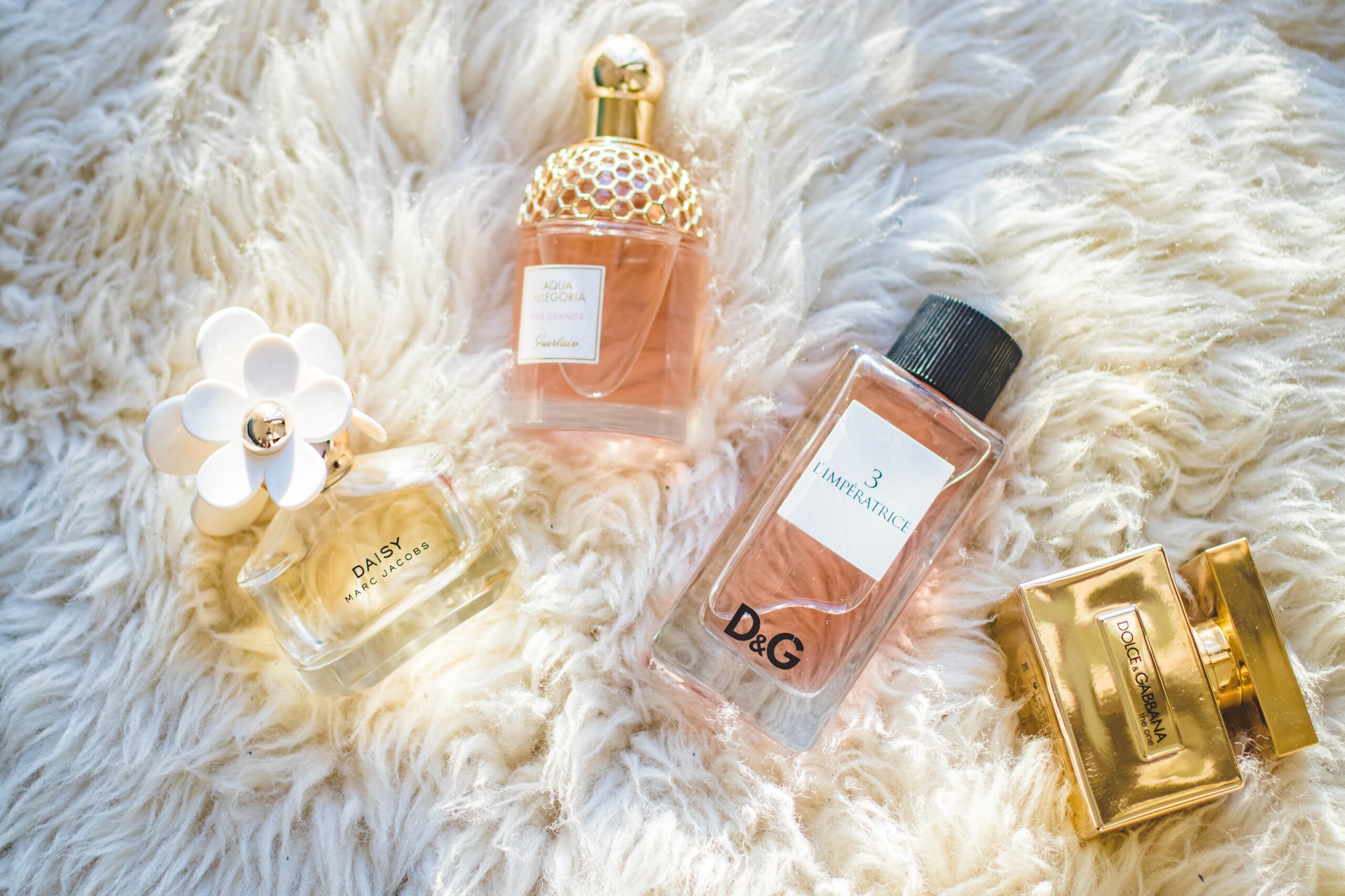 A variety of luxury perfumes are laid on a fuzzy, white garment.