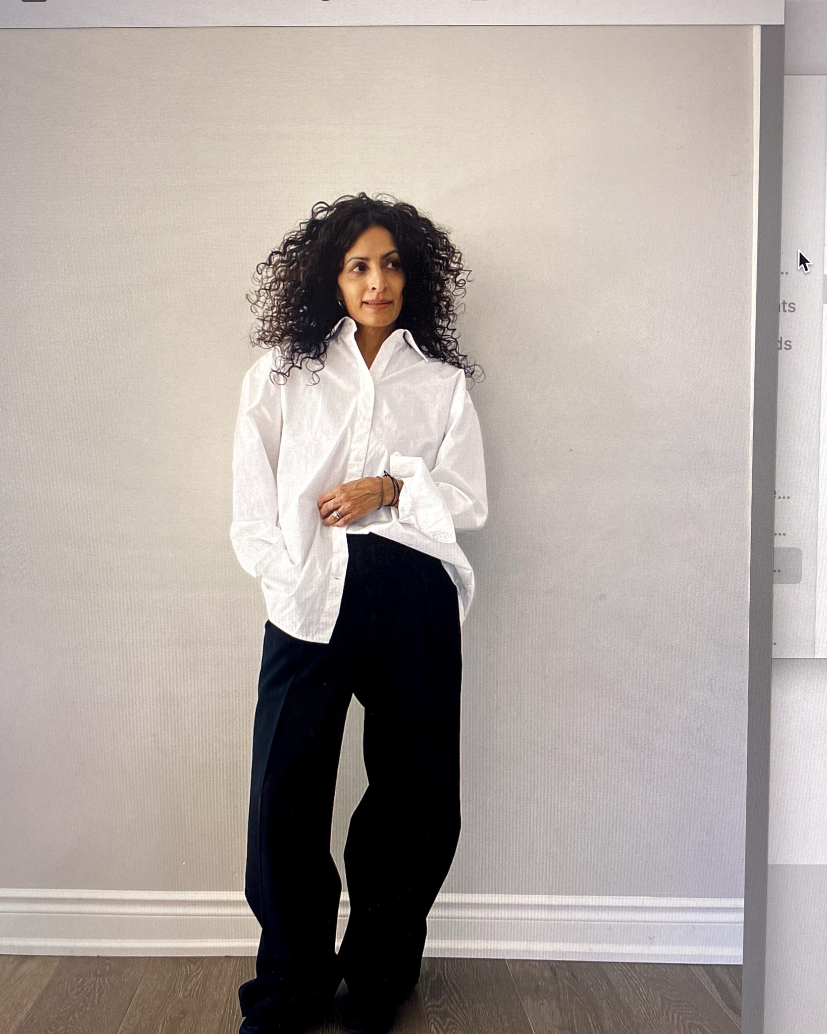 A woman stands against the wall wearing a white button up shirt and black pants from Aritzia.