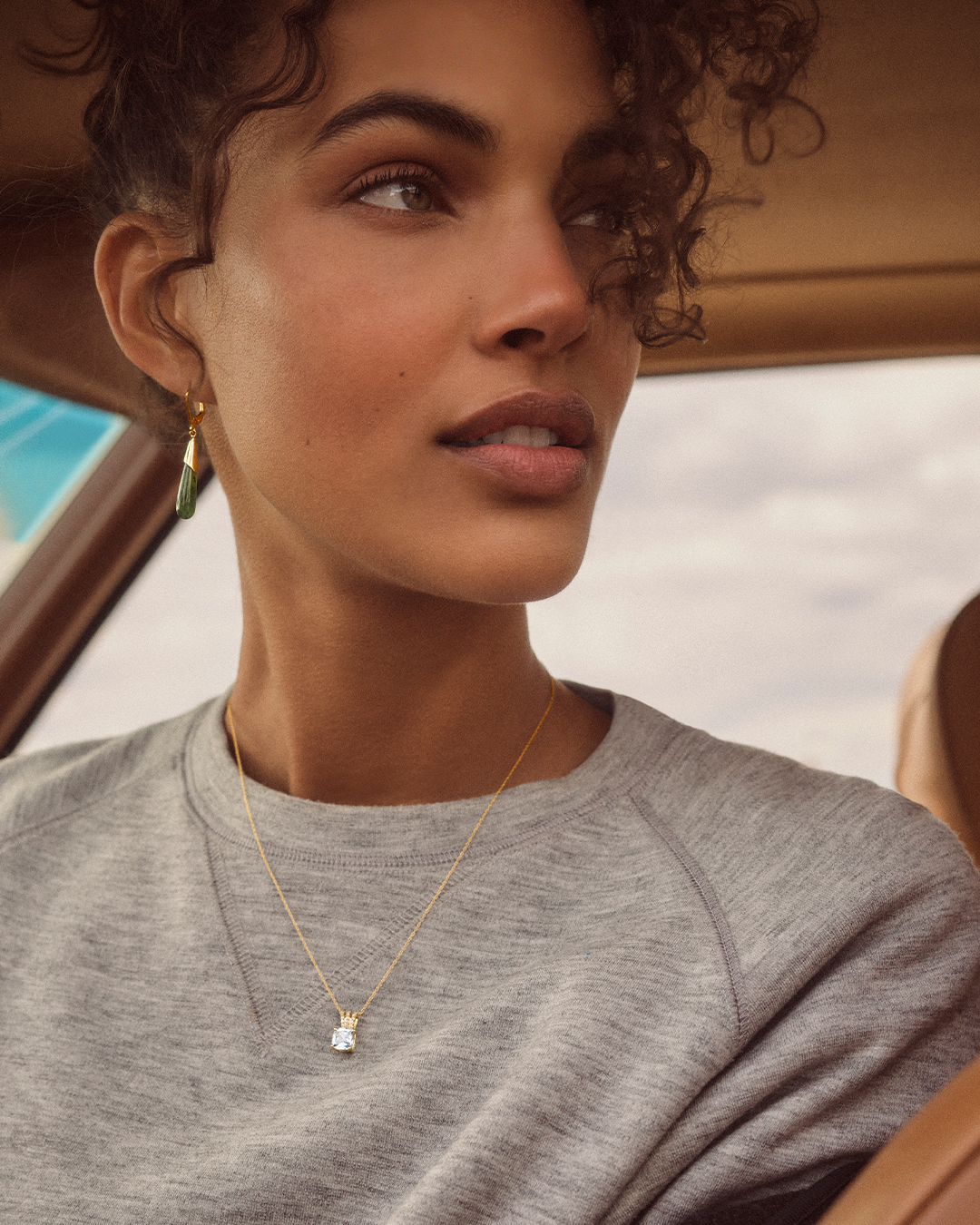 A woman sits in the car and shows off earrings and a necklace from Peoples Jewellers.