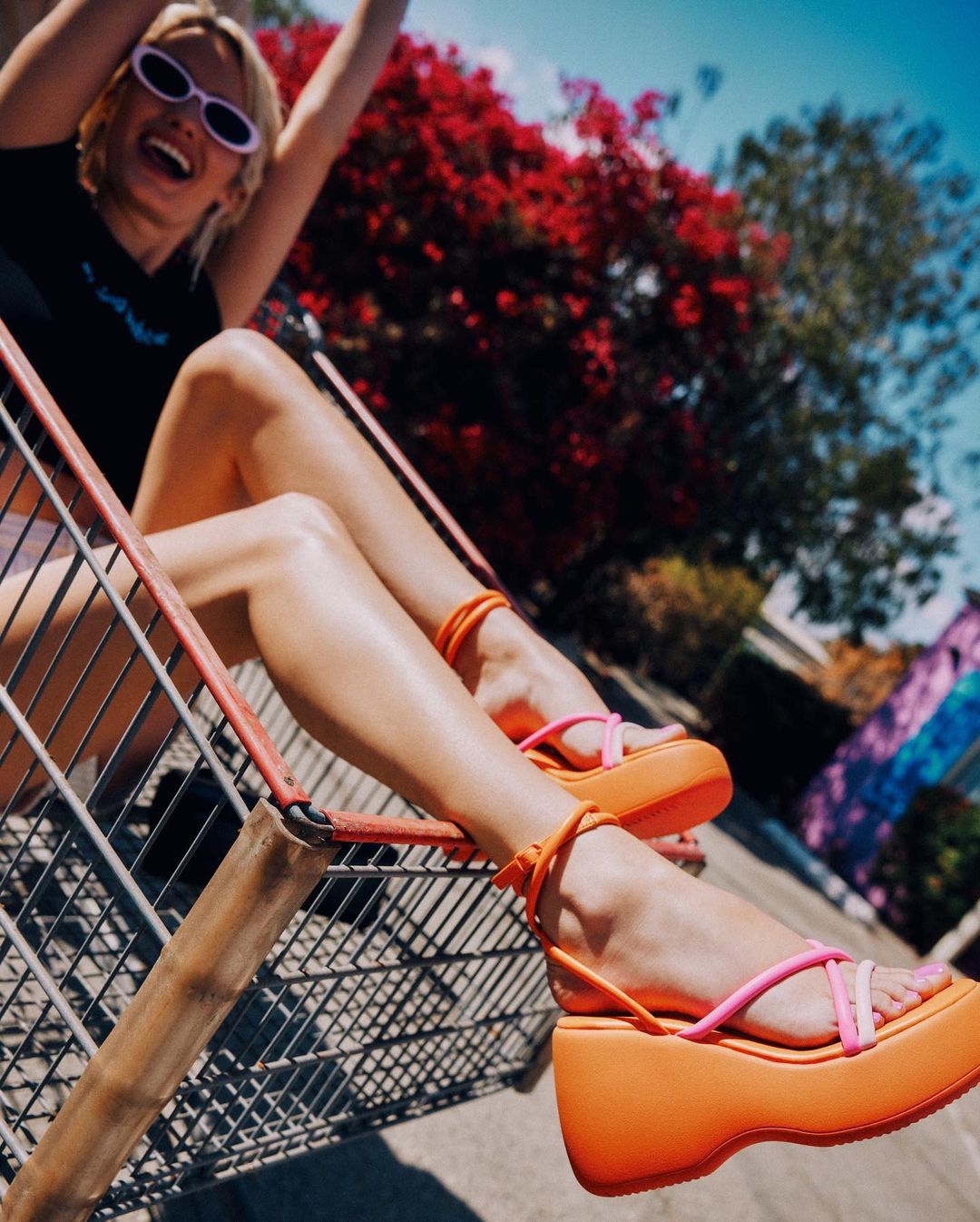 image of a woman posing in a shopping cart showing off orange and pink wedge sandals