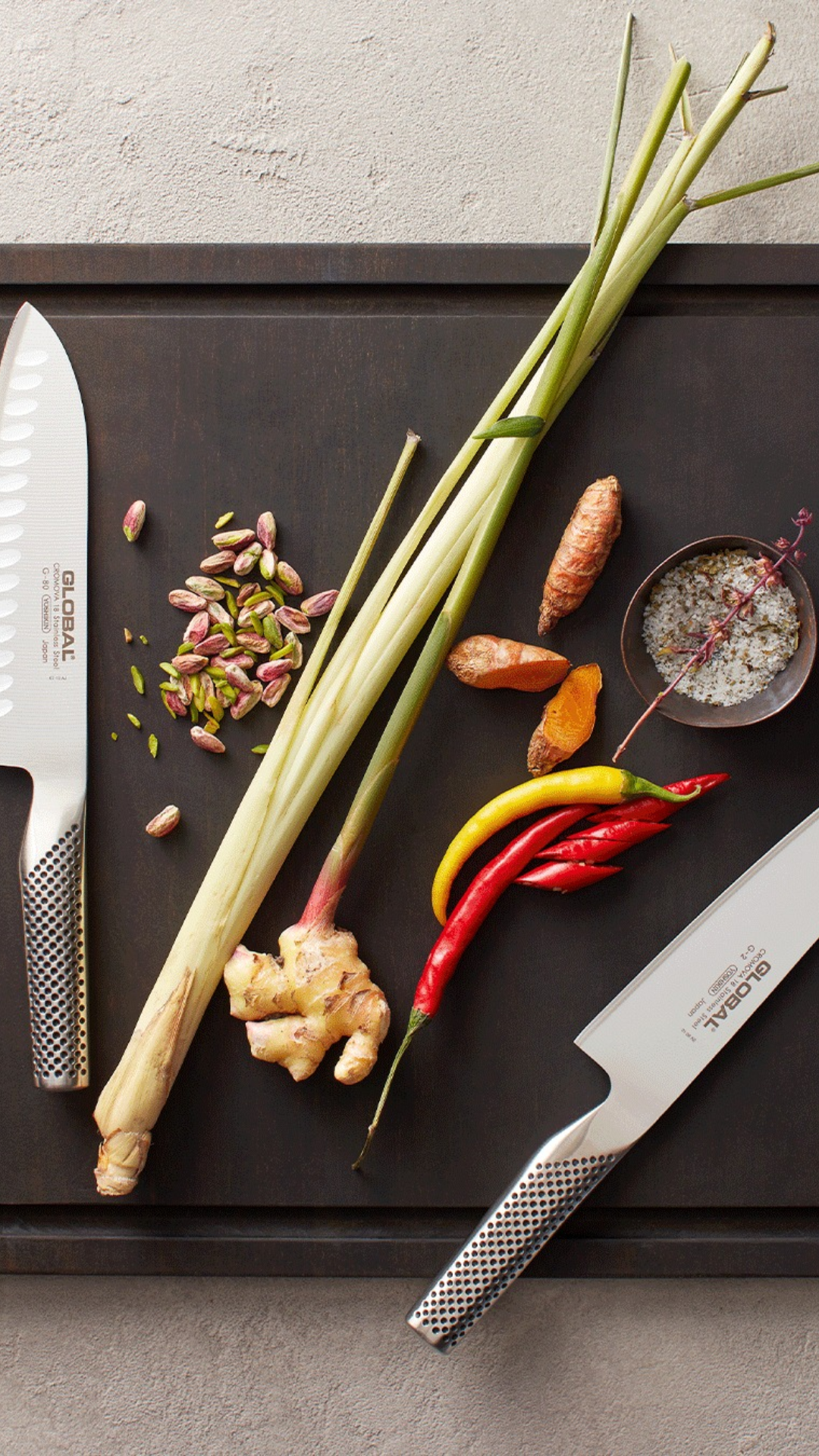 flat lay of a black cutting board with two knives, peppers, ginger, scallions, seeds and salt