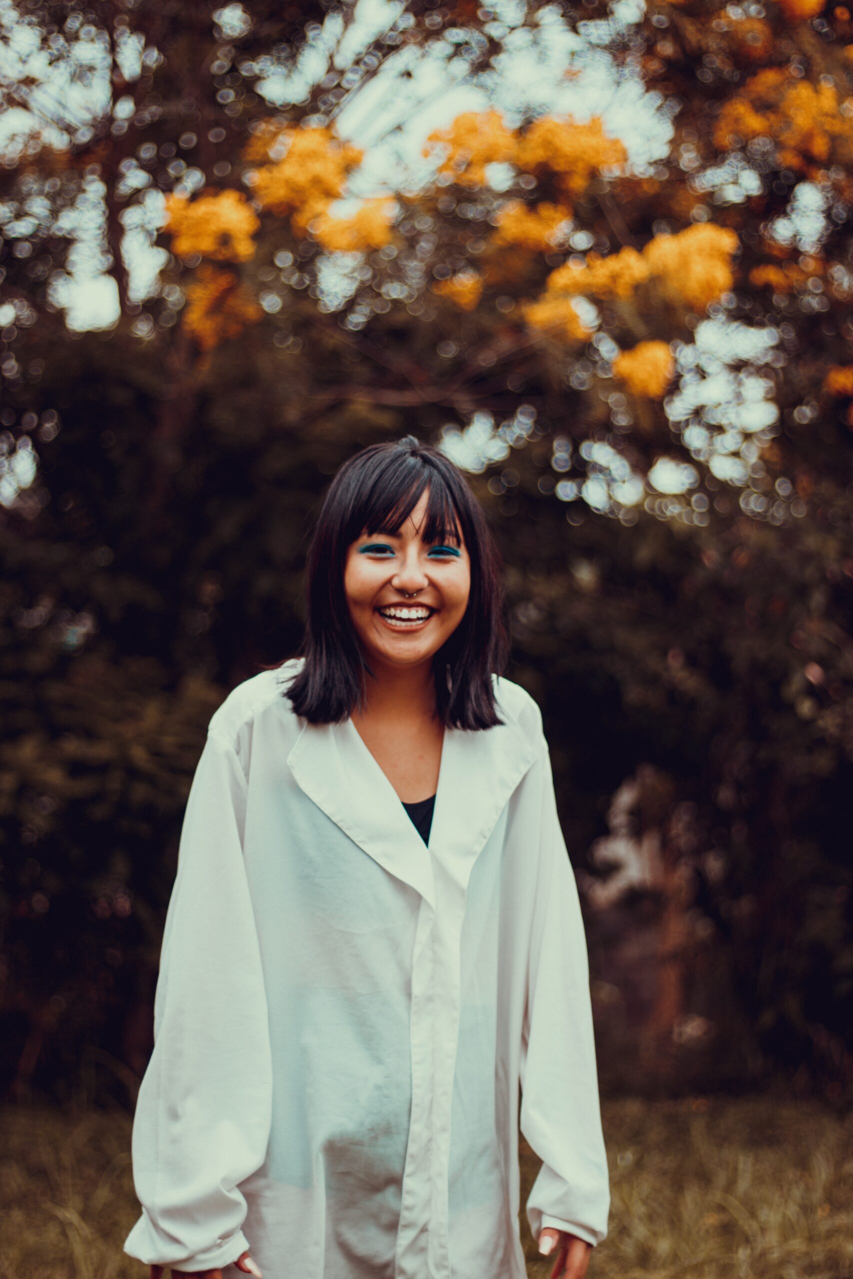 A person wearing a white blouse smiling at camera in a fall setting.