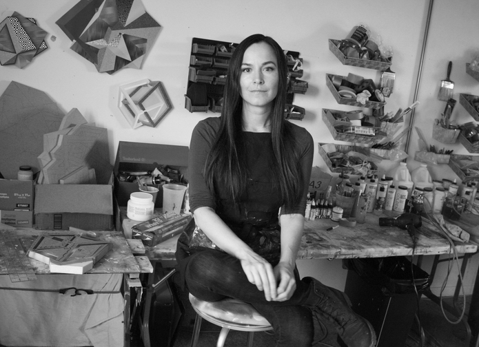 Laura Payne sitting on a stool in a room with persony objects on the wall