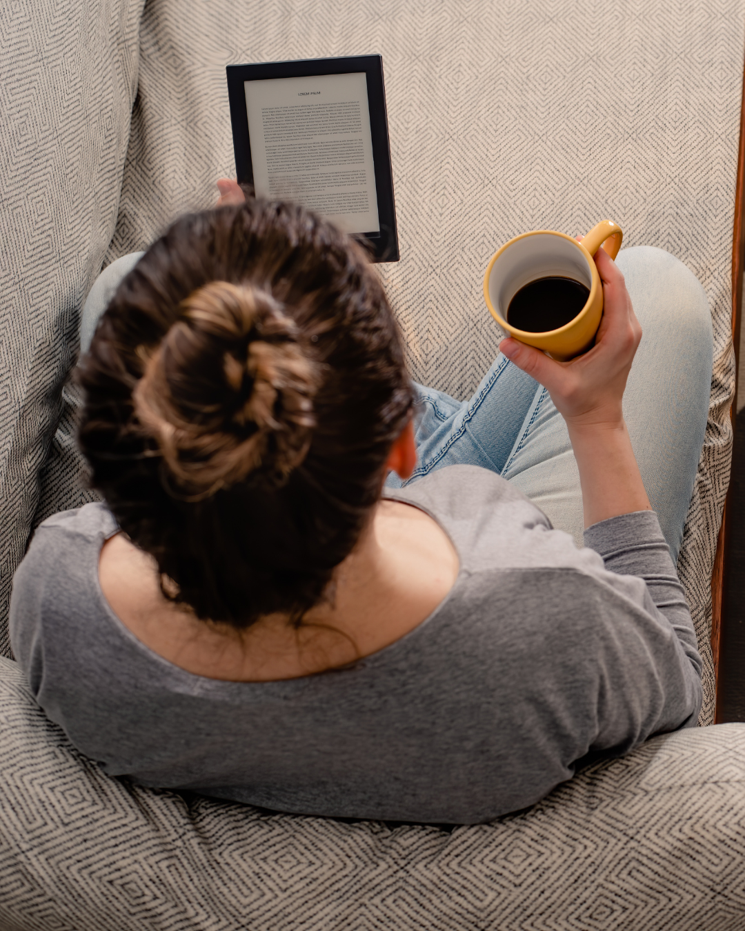 a person sitting on a couch holding a coffee cup and a tablet