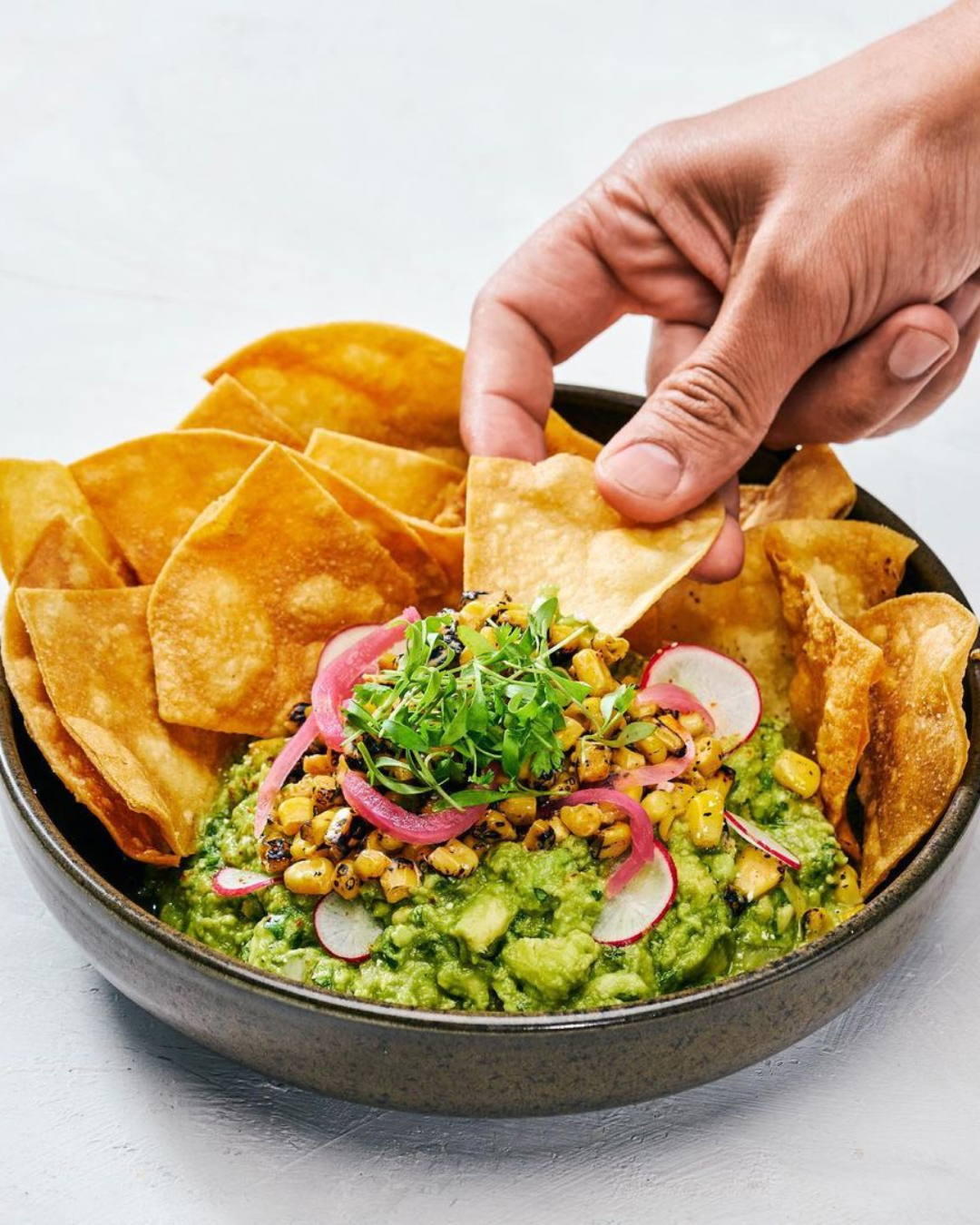 a person dipping a chip into a bowl of guacamole