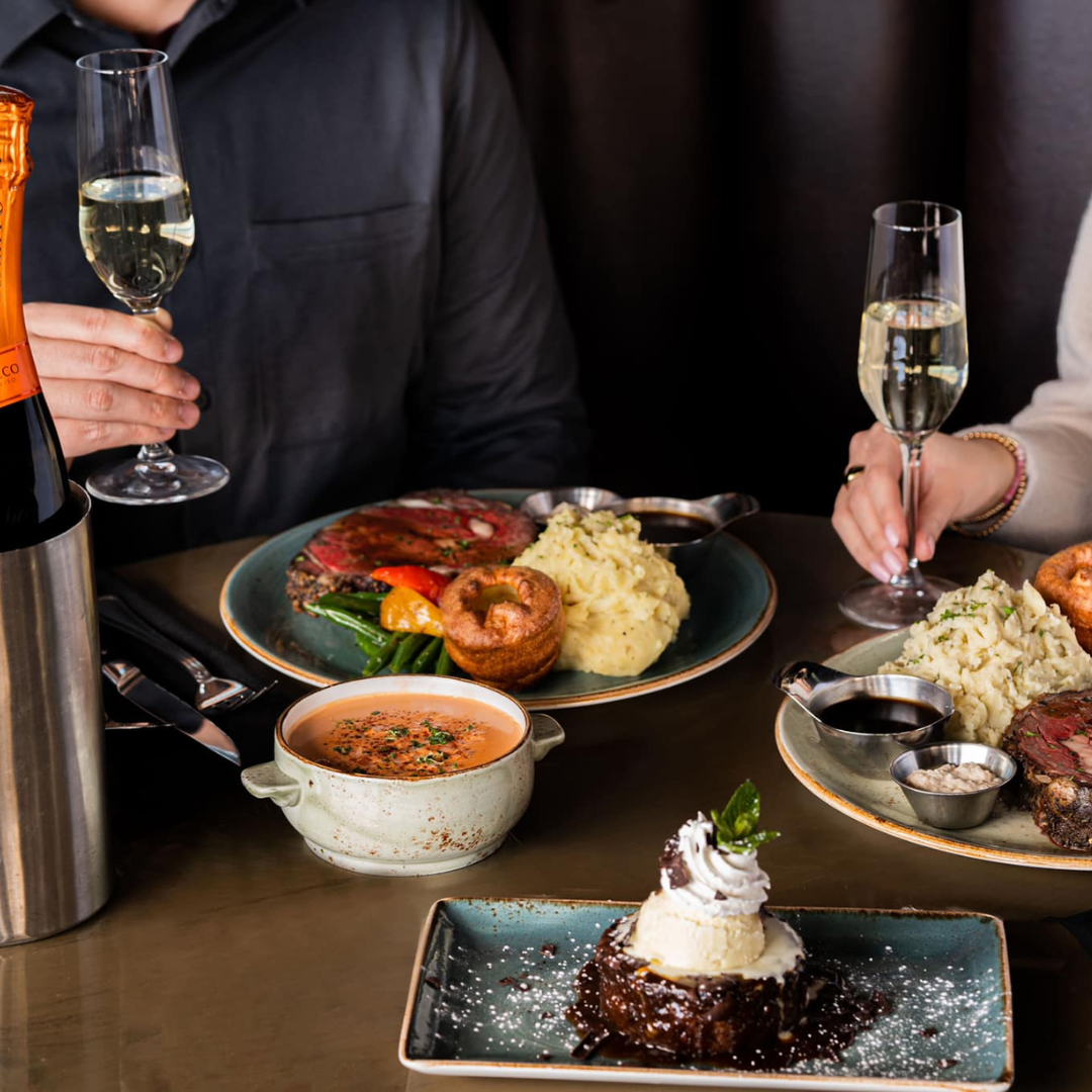 food on table with two people holding wine glasses