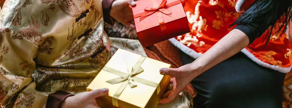 a pair of hands holding a gold and red gift box