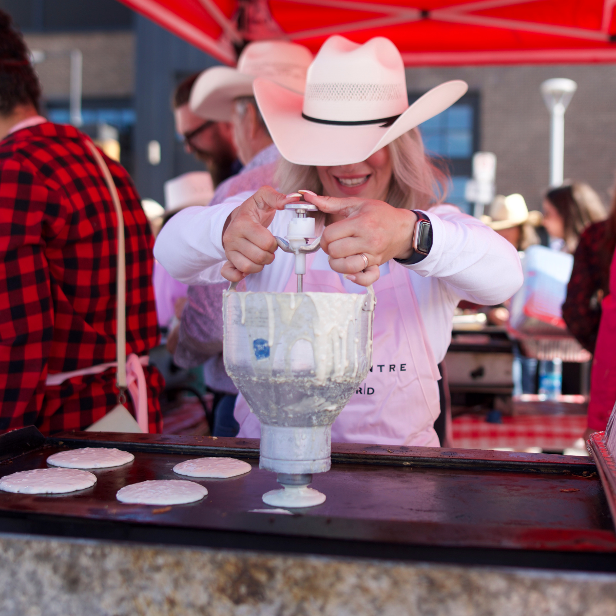woman in cowboy hate and pink apron making pink pancakes on griddle