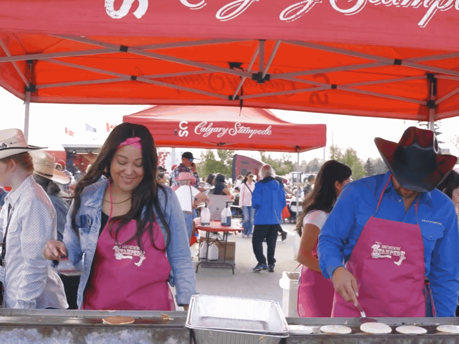 two people flipping pancakes wearing pink aprons