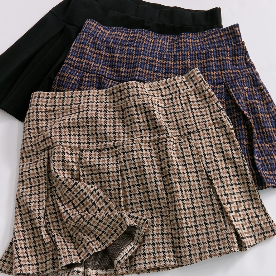 Three different plaid skirts in black, navy blue, and beige houndstooth patterns laid out on a flat surface