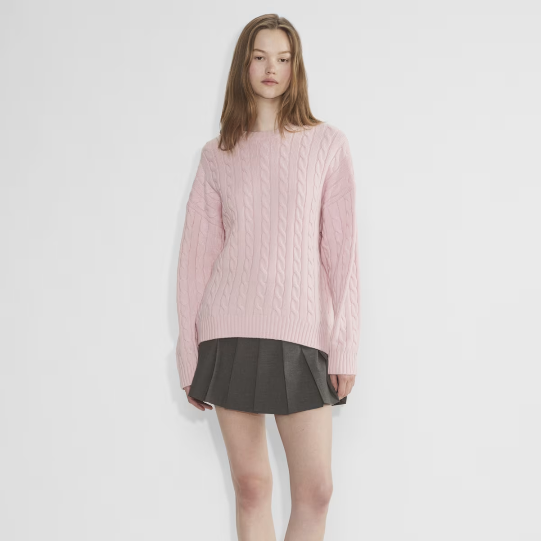 Woman wearing a pink cable knit sweater and pleated gray skirt